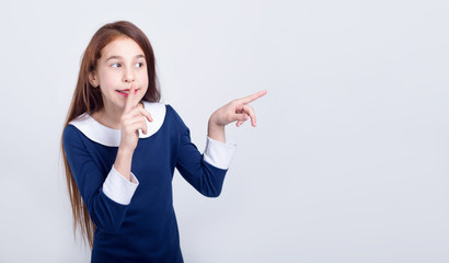 Girl with long red hair shows hush sign. Schoolgirl pointing and whispering a secret.