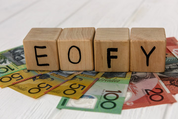 Wooden cubes with letters EOFY on australian dollar banknotes