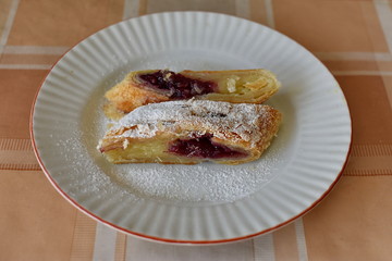 Two slices of tasty cherry strudel with vanilla cream on the plate