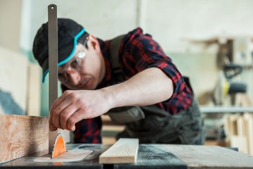 The worker makes measurements of a wooden board with corner ruler.