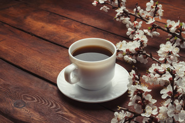 Sakura branches with flowers and a white cup with a black coffee on a dark wooden background. Concept of Spring
