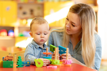 Baby minder playing with kid in nursery. Developmental toys for preschool.