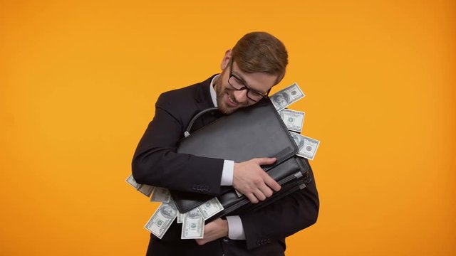 Businessman hugging briefcase full of money, isolated on yellow background