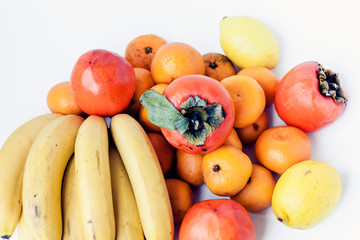 A selection of arranged different fresh fruits of bananas, mandarins, persimmons and lemons on white background close up.