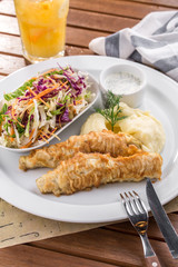 crispy fried fish and mashed potatoes with vegetable salad on wooden table