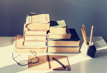 Stack of old books, textbook, glasses and pencils in office background for education retro concept.