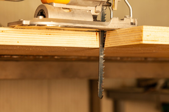 A yellow electric jigsaw ready for use stands in a sawn wood building material on a workbench in a workshop for carpentry work. Tool for industry and production.