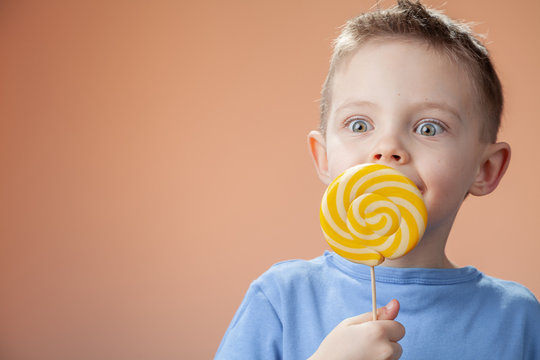  Beautiful cute boy with yellow candy on a bright background.