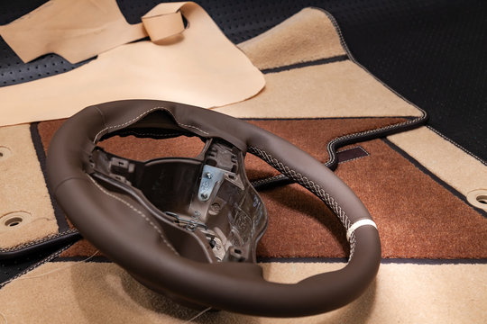 Leather steering wheel brown color in the process of stitching with a bright contrast seam and white central point on the top in the workshop for the repair of car interiors and tuning design