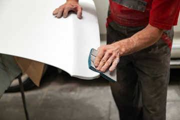 Preparation for painting a car element using emery sponge by a service technician leveling out...
