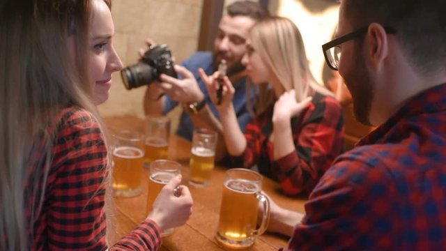 a group of friends - young guys and girls drinking beer, talking and smiling at the bar