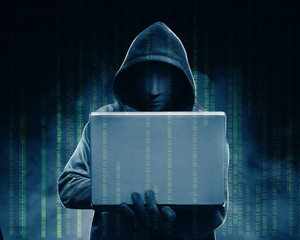 Hacker in black hoodie holding laptop with his hand and binary code