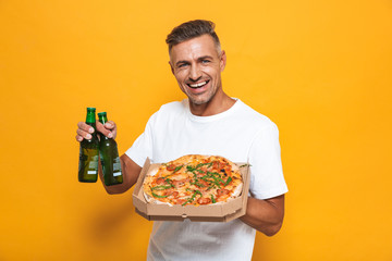 Image of adult man 30s in white t-shirt drinking beer and eating pizza while standing isolated