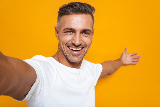 Image of happy man 30s in white t-shirt smiling and taking selfie photo