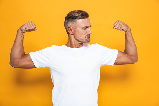 Image of beautiful man 30s in white t-shirt raising hands and showing biceps
