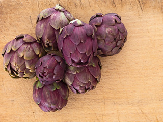Raw artichokes, Mediterranean vegetable, uncooked on wooden board. Closeup.