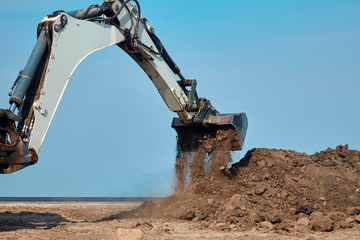 Excavator loader working at ground area on blue sky background, digging process. Bucket up scoops ground.. Outdoors, copy space.