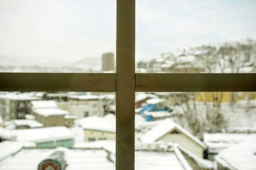 Closeup wooden frame of window and glass with blurry outside view of snow capped city and winter blue sky background.