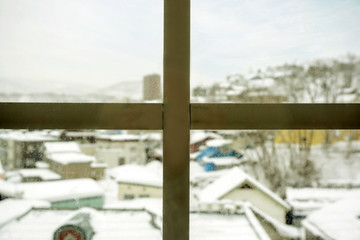 Fototapeta premium Closeup wooden frame of window and glass with blurry outside view of snow capped city and winter blue sky background.