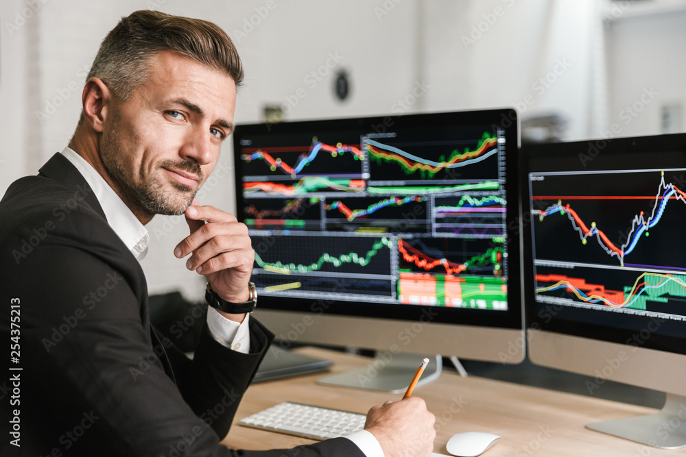 Wall mural portrait of confident businessman sitting in office and working with digital graphics on computer