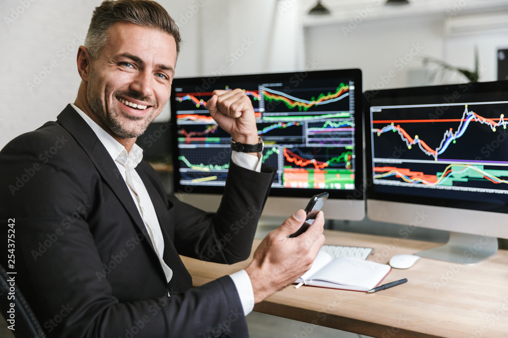 Poster portrait of male mentor using mobile phone while working with digital graphics on computer in office