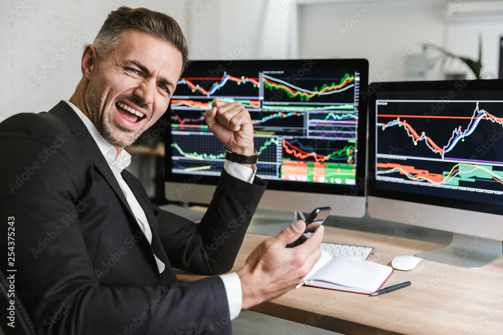 Poster portrait of male employee using mobile phone while working with digital graphics on computer in offi