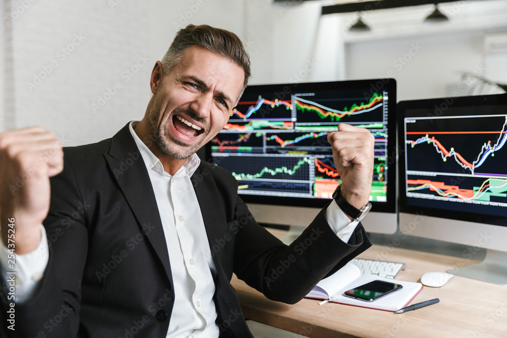 Poster photo of ecstatic businessman rejoicing while working in office with digital graphics and charts