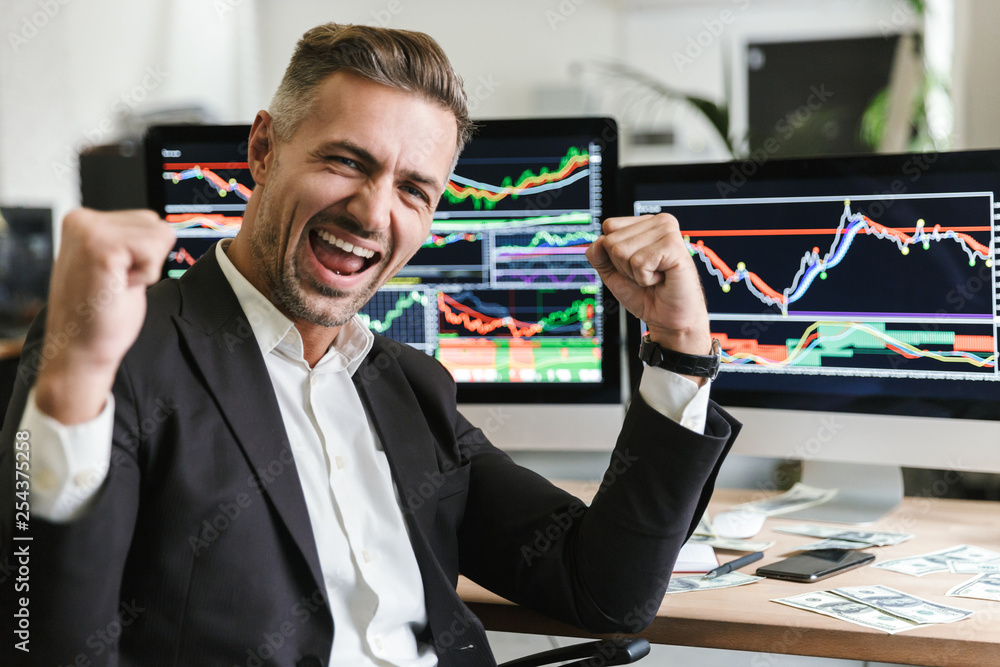 Poster photo of confident businessman rejoicing while working in office with digital graphics and charts