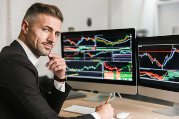 Portrait of confident businessman sitting in office and working with digital graphics on computer