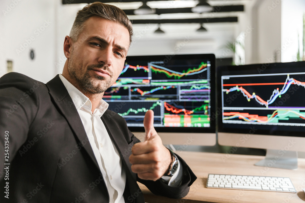 Poster photo of businesslike man taking selfie while working in office on computer with graphics and charts