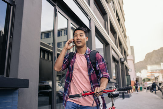 Young man walking with his bicycle talking on a cellphone