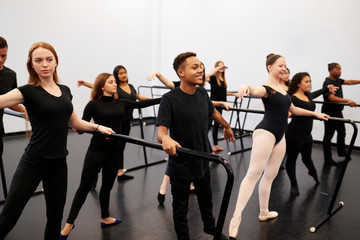Male And Female Students At Performing Arts School Rehearsing Ballet In Dance Studio Using Barre