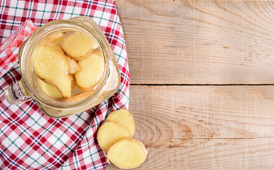 Opened glass jar with ginger water on red tartan cloth on wooden planks. 