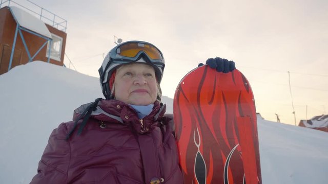 Senior woman posing with snowboard on the mountain peak. Concentrated senior woman with snowboard on the mountain peak looking in front, before her ride down the snowy hill.