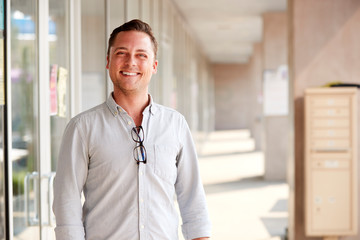 Portrait Of Smiling Male School Teacher Standing In Corridor Of College Building