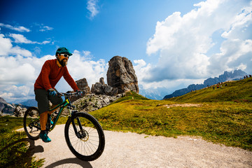 Tourist cycling in Cortina d'Ampezzo, stunning Cinque Torri and Tofana in background. Man riding MTB enduro flow trail. South Tyrol province of Italy, Dolomites.