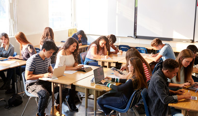 Wide Angle View Of High School Students Sitting At Desks In Classroom Using Laptops