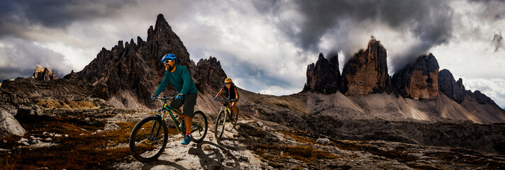 Cycling woman and man riding on bikes in Dolomites mountains andscape. Couple cycling MTB enduro trail track. Outdoor sport activity.