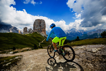 Tourist cycling in Cortina d'Ampezzo, stunning Cinque Torri and Tofana in background. Man riding MTB enduro flow trail. South Tyrol province of Italy, Dolomites.