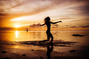 Woman walk on the beach on the sunset. Bright colors in the evening.