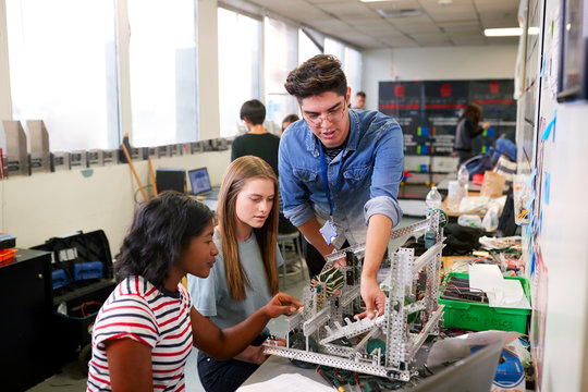 Teacher With Two Female College Students Building Machine In Science Robotics Or Engineering Class