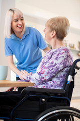 Obraz premium Female Care Assistant Talking To Senior Woman Sitting In Wheelchair At Home