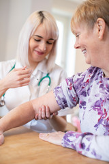 Female Nurse Giving Senior Woman Injection In Arm With Syringe