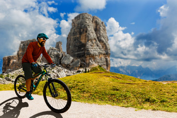 Tourist cycling in Cortina d'Ampezzo, stunning Cinque Torri and Tofana in background. Man riding MTB enduro flow trail. South Tyrol province of Italy, Dolomites.
