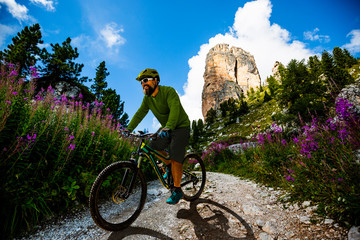 Tourist cycling in Cortina d'Ampezzo, stunning Cinque Torri and Tofana in background. Man riding MTB enduro flow trail. South Tyrol province of Italy, Dolomites.