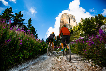 Cycling woman and man riding on bikes in Dolomites mountains landscape. Couple cycling MTB enduro trail track. Outdoor sport activity.