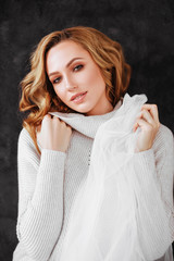 Studio shot of beautiful young woman with blonde hair wearing loose long-sleeved sweater over white dress. Beauty and youth