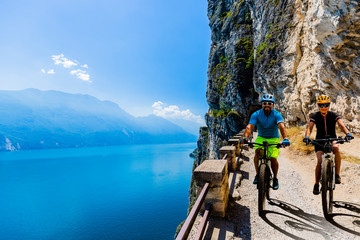 Cycling woman and man riding on bikes at sunrise mountains and Garda lake landscape. Couple cycling...