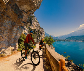 Cycling woman and man riding on bikes at sunrise mountains and Garda lake landscape. Couple cycling MTB enduro flow sentiero ponale trail track. Outdoor sport activity.