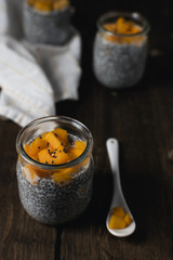 Chia pudding in glass jar with almond milk and mango on rustic wooden table